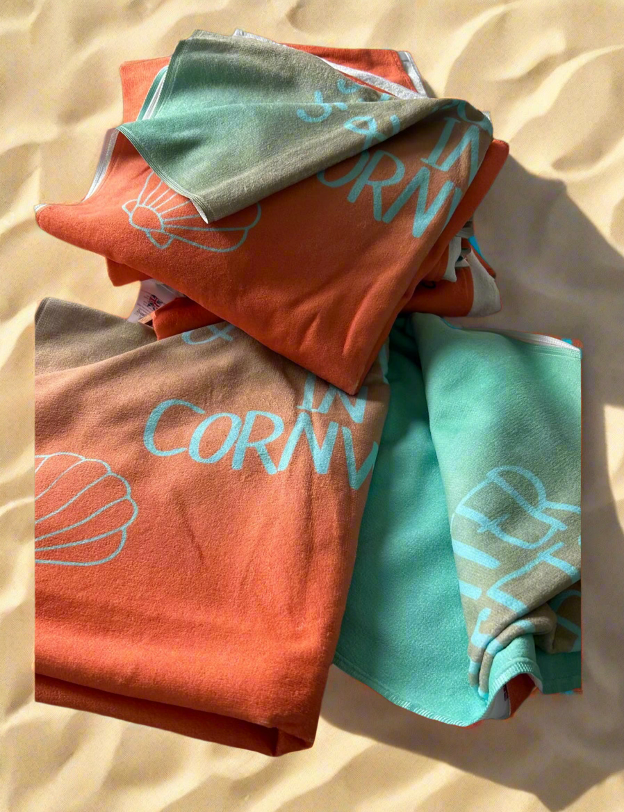 alt=“Lightweight, quick-drying mint and orange microfibre beach towel with the slogan ‘Saltwater & Sunsets in Cornwall’ in bold white text – perfect for beach days”