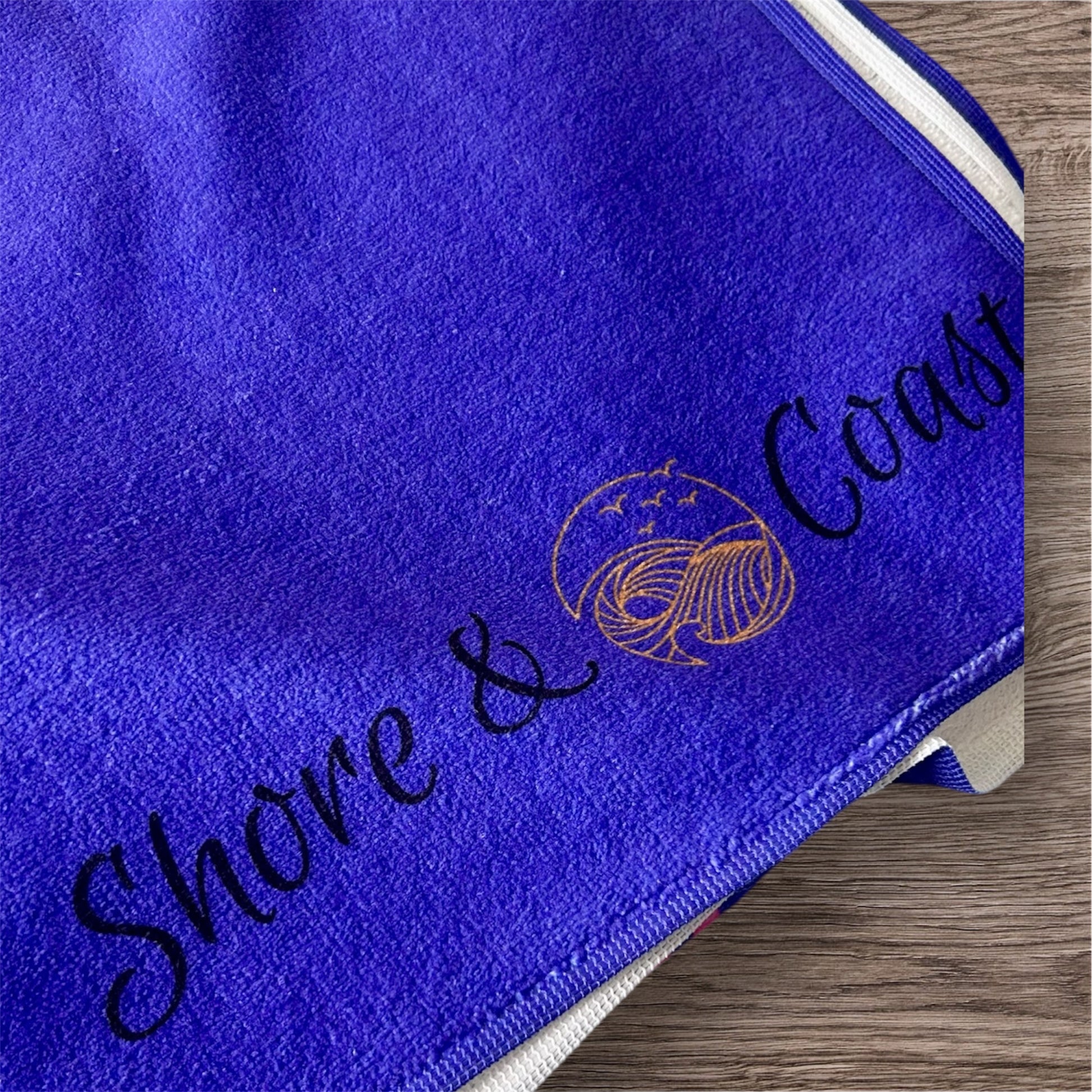 alt=“Purple microfibre beach towel with cotton loops and the slogan ‘Life is better in Anglesey’ in bold pink text – ultra-absorbent, quick-drying, and perfect for seaside adventures”