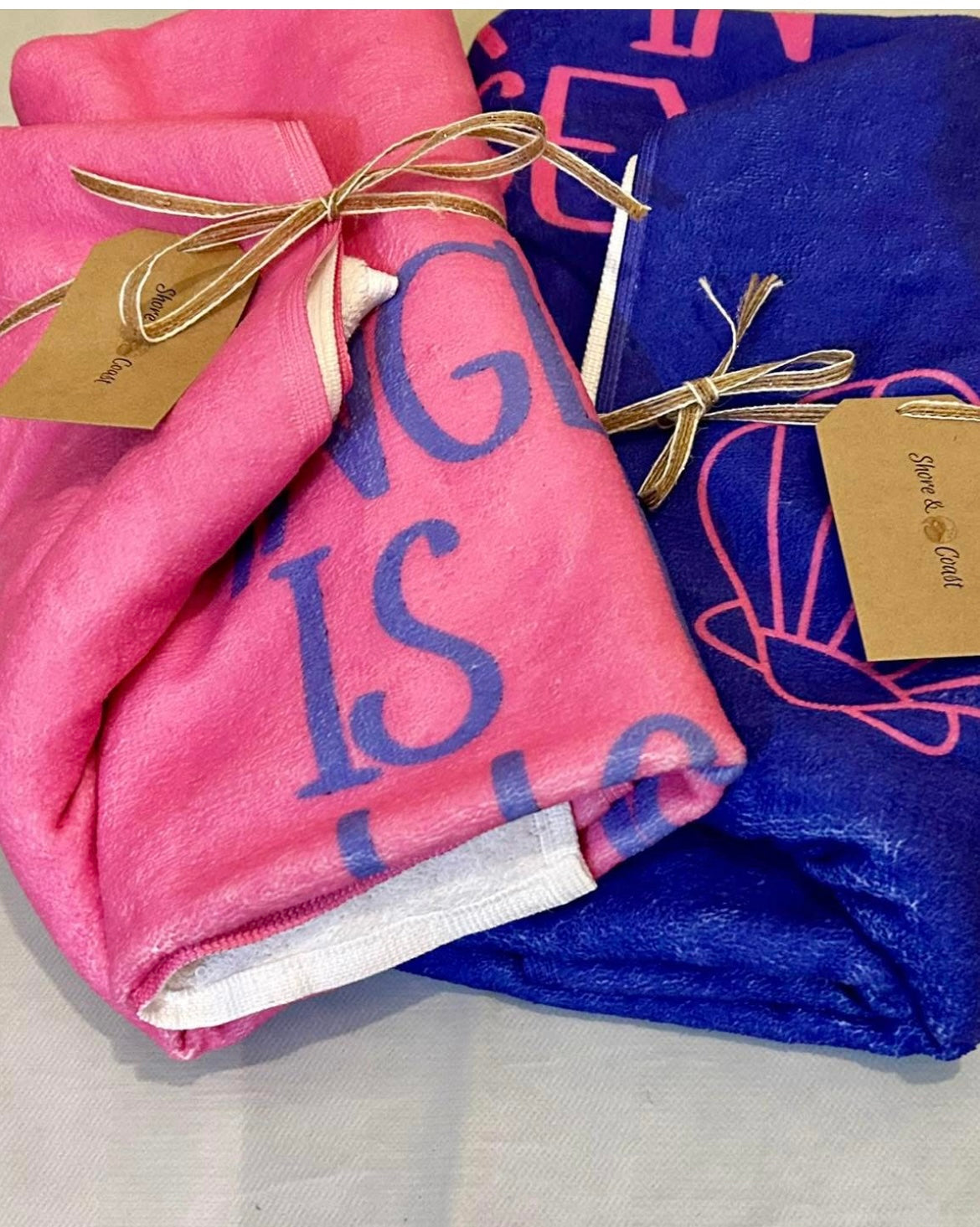 alt=“Pink microfibre beach towel with the slogan ‘Anglesey is my happy place’ in bold white text – lightweight, quick-drying, and perfect for coastal days with Shore & Coast”