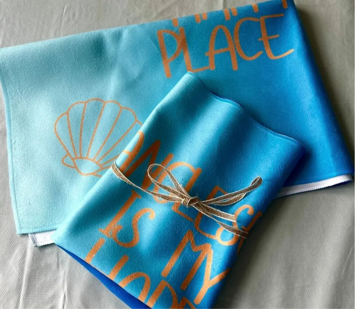 alt=“Quick-drying and absorbent microfibre tea towel with ‘Anglesey is my happy place’ slogan – ideal for beach lovers and coastal kitchens