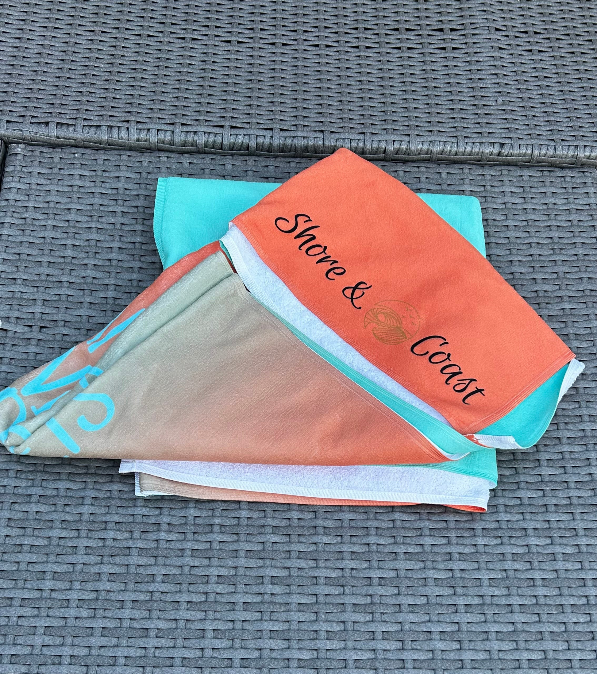 alt=“Mint and orange ombré microfibre beach towel with the slogan ‘Life is better in Anglesey’ in bold white text”