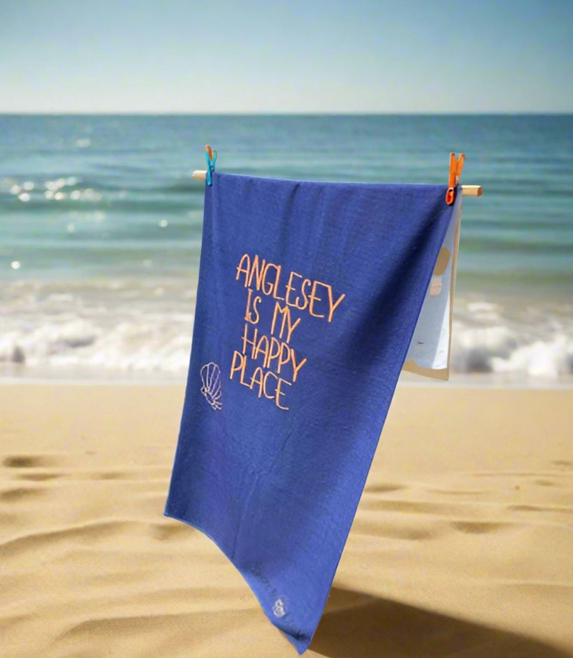 alt=“Navy microfibre beach towel with cotton loops featuring the slogan ‘Anglesey is my happy place’ in bold orange text – quick-drying, absorbent, and perfect for the coast”