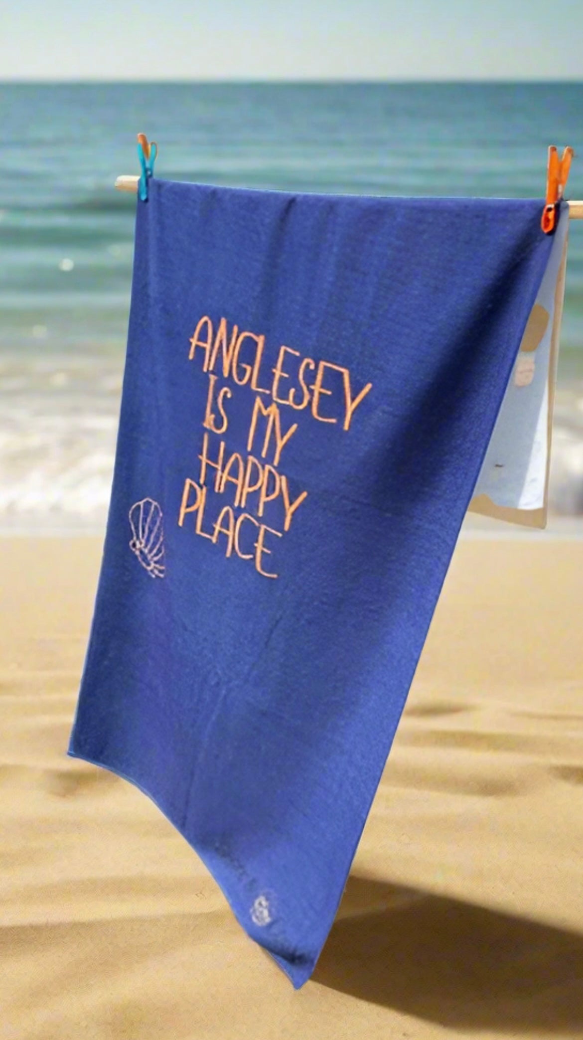 alt=“Navy microfibre beach towel with cotton loops featuring the slogan ‘Anglesey is my happy place’ in bold orange text – quick-drying, absorbent, and perfect for the coast”