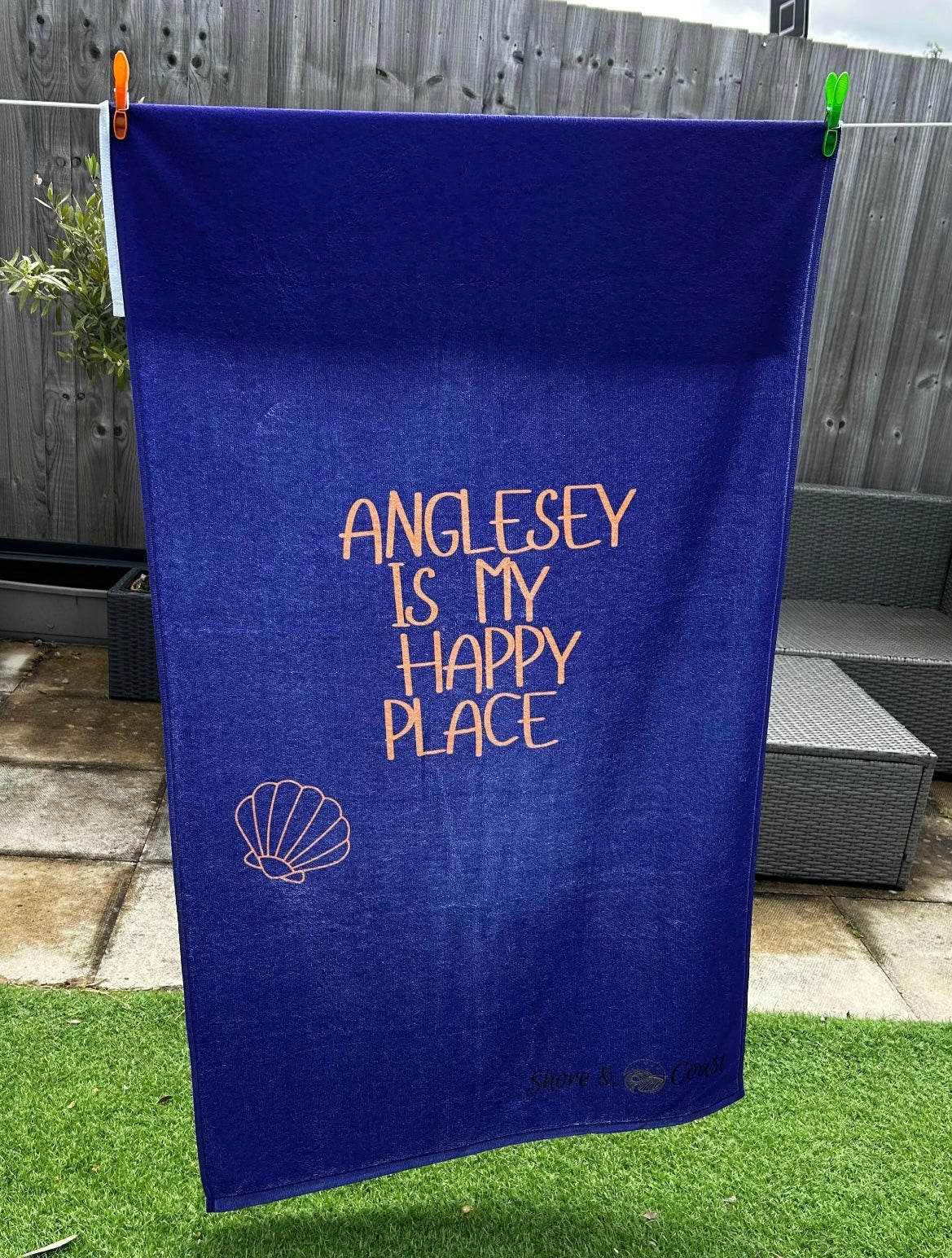 alt=“Navy microfibre beach towel with cotton loops featuring the slogan ‘Anglesey is my happy place’ in bold orange text – quick-drying, absorbent, and perfect for the coast”