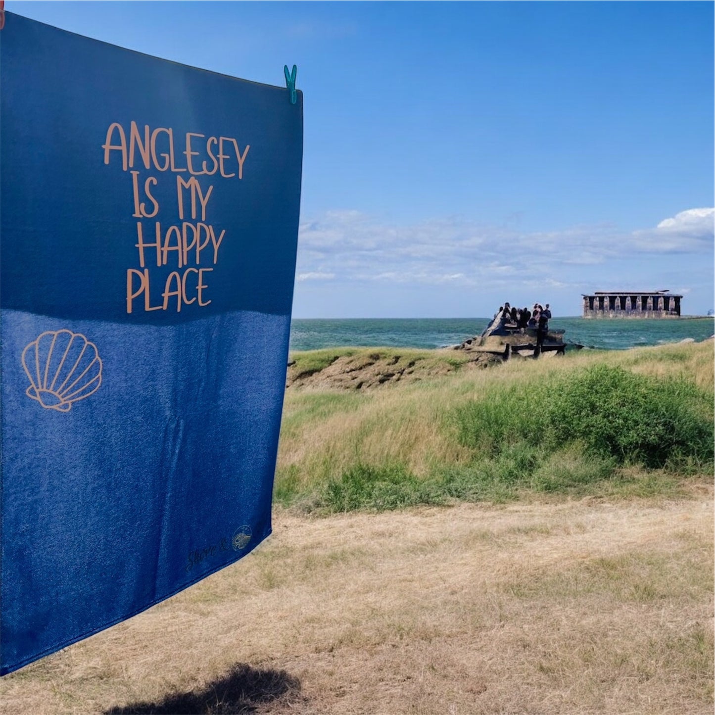 alt=“Navy microfibre beach towel with cotton loops featuring the slogan ‘Anglesey is my happy place’ in bold orange text – quick-drying, absorbent, and perfect for the coast”