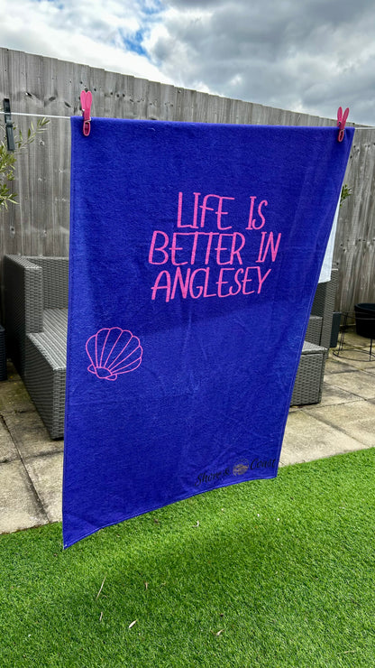 alt=“Purple microfibre beach towel with cotton loops and the slogan ‘Life is better in Anglesey’ in bold pink text – ultra-absorbent, quick-drying, and perfect for seaside adventures”